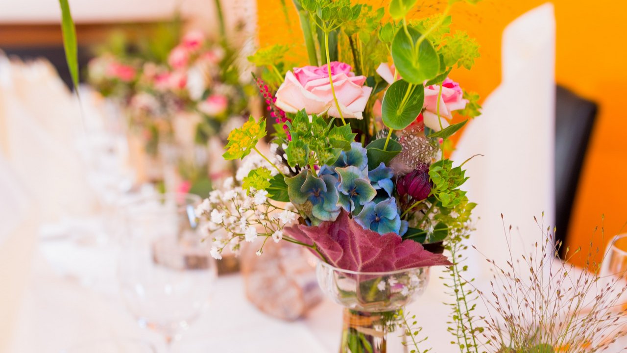 Blumenstrauß mit Rosen und verschiedenen Blumendekorationen auf eingedecktem Tisch