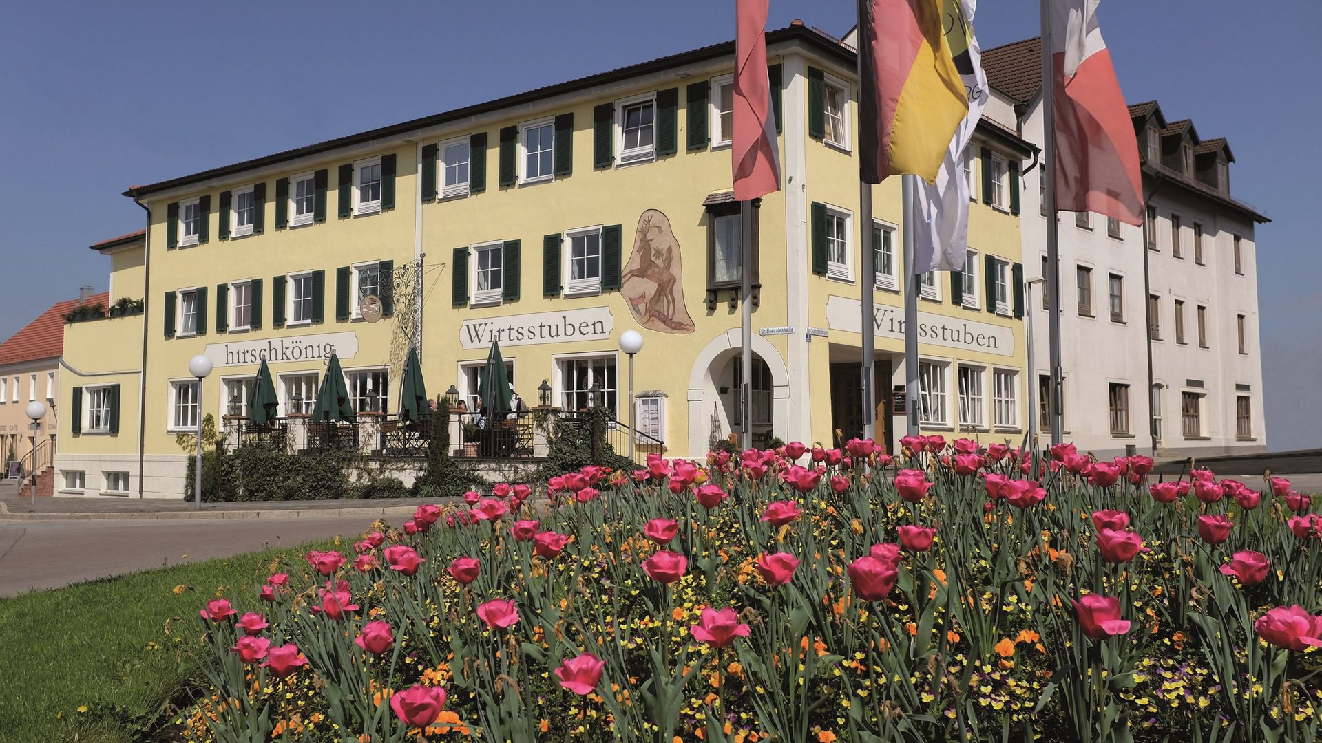 Romantik Hotel Hirschen: Blog Gelbes Gasthaus mit grünen Fenstern, roten Tulpen im Vorgarten und wehenden Fahnen