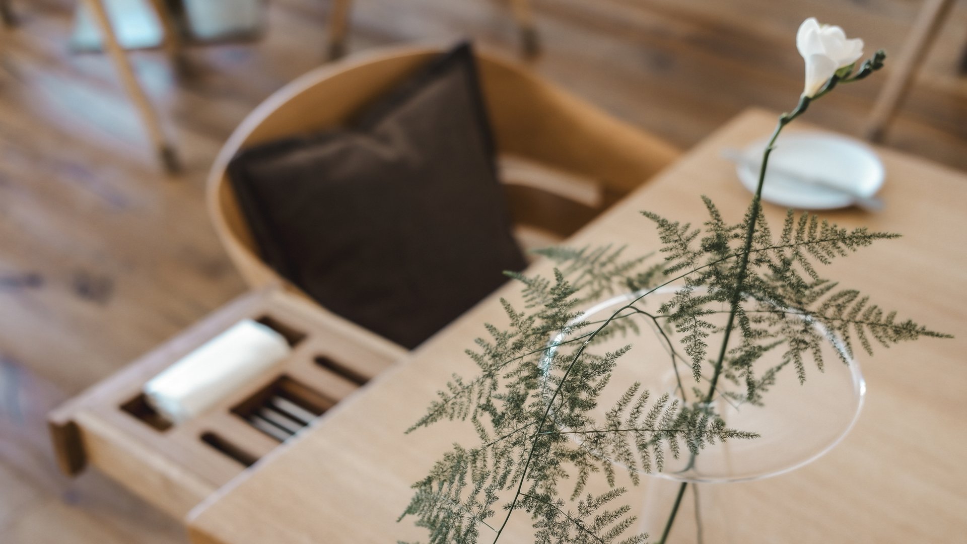 Restaurant in Parsberg: Gourmet genießen Weiße Blume und Farn in Glasvase auf Holztisch neben Stuhl mit braunem Kissen