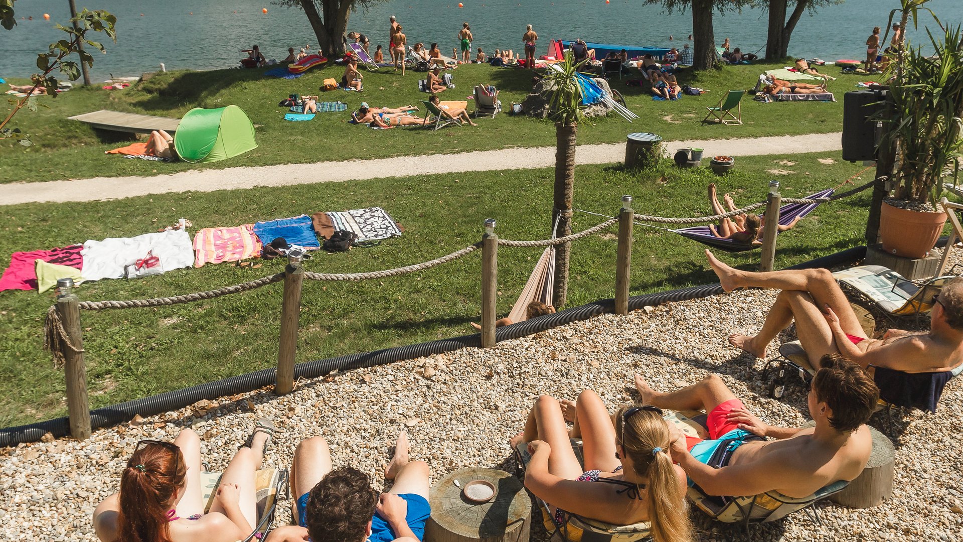Badeseen Menschen entspannen am Seeufer auf Liegestühlen und Wiesen unter blauem Himmel
