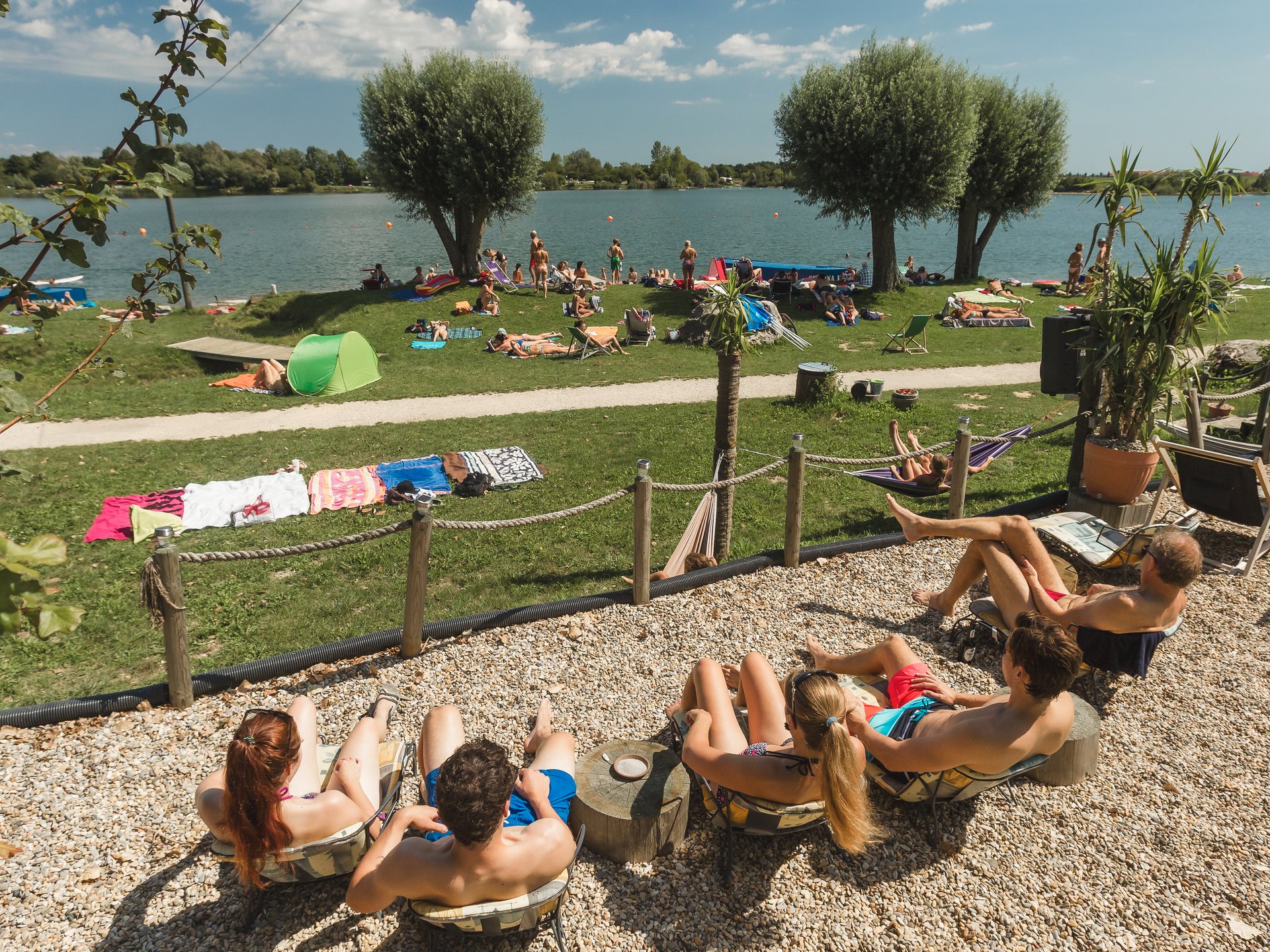 Badeseen Menschen entspannen am Seeufer auf Liegestühlen und Wiesen unter blauem Himmel