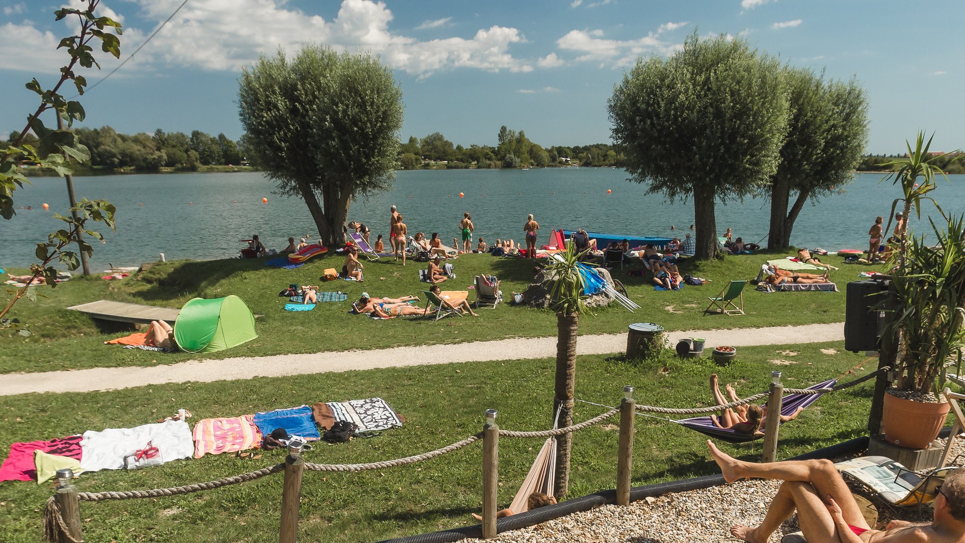 Badeseen Menschen entspannen am Seeufer auf Liegestühlen und Wiesen unter blauem Himmel