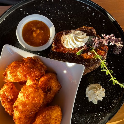 Beer garden in Parsberg: HirschenBlobb Grilled steak with herb butter, apple sauce, and fried potatoes on a black plate