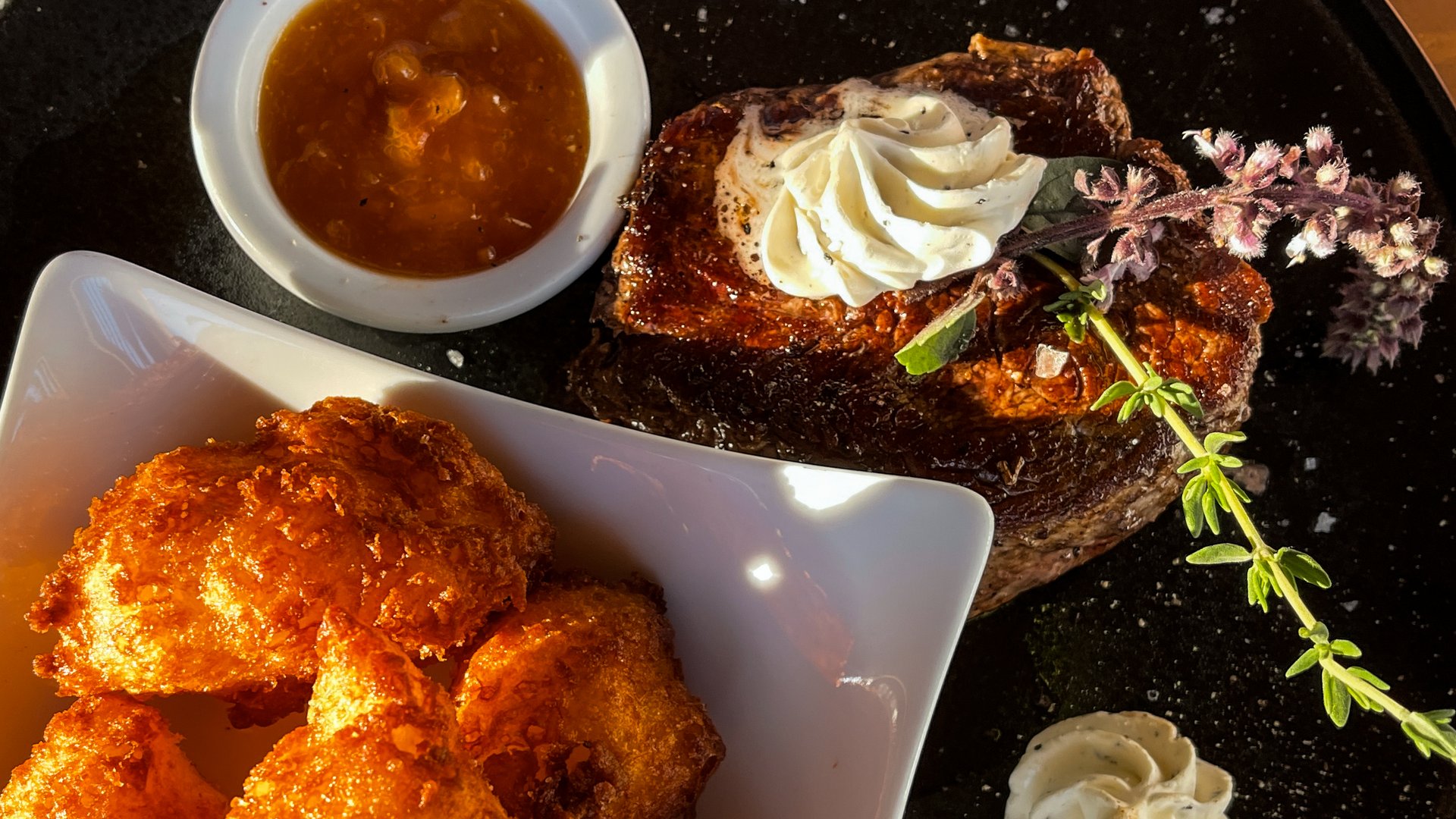 Beer garden in Parsberg: HirschenBlobb Grilled steak with herb butter, apple sauce, and fried potatoes on a black plate
