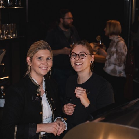 Hirschenblobb: Our bar Two smiling waitresses behind bar with drinks and customers in background