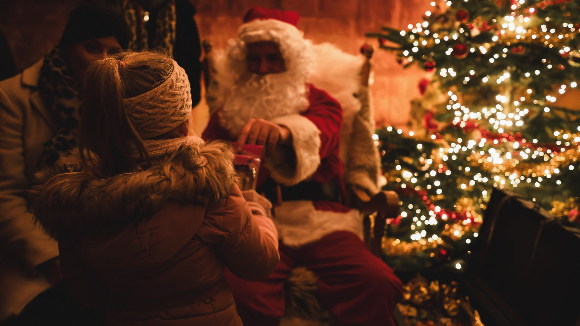 Weihnachtsmärkte Weihnachtsmann sitzt neben einem Kind vor einem beleuchteten Weihnachtsbaum
