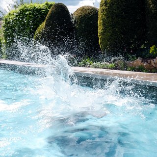 Home Wasserspritzer nach einem Sprung in den Pool mit gepflegten Hecken im Hintergrund