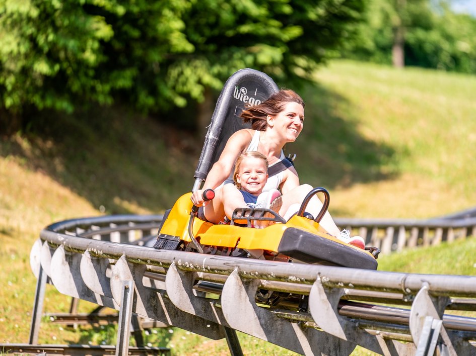 Wandern in der Oberpfalz: Aktiv in der Natur Frau und Kind fahren lachend auf einer Sommerrodelbahn im Grünen