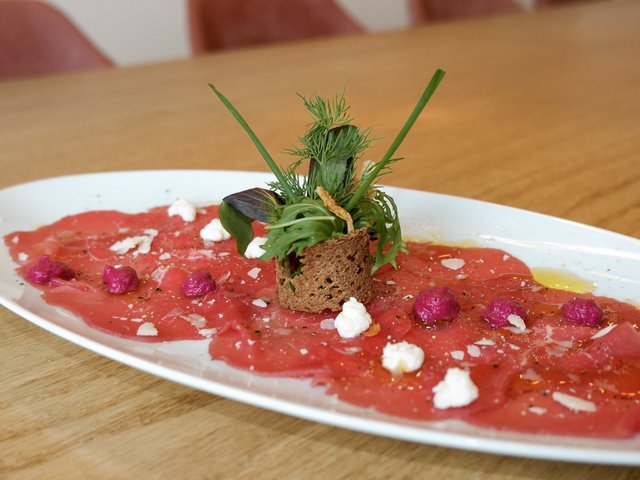 Romantik Hotel Hirschen: Bildergalerie Rindercarpaccio mit Kräutern und kleinen Frischkäsetupfen auf weißem Teller