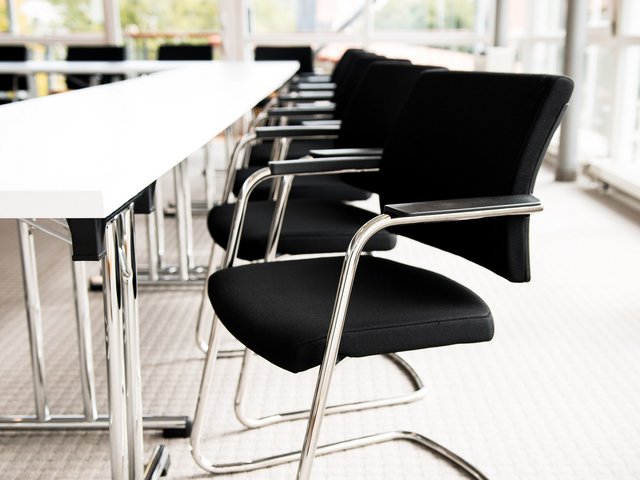 Romantik Hotel Hirschen: Bildergalerie Leere schwarze Stühle an einem weißen Besprechungstisch in einem hellen Raum