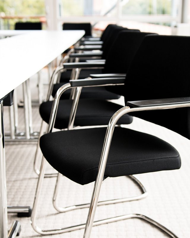 Looking for somewhere for conferences in Bavaria? Empty black chairs along a white conference table in a bright room