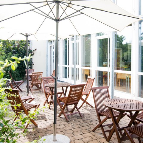 Looking for somewhere for conferences in Bavaria? Patio with wooden tables, chairs, and large umbrellas in daylight