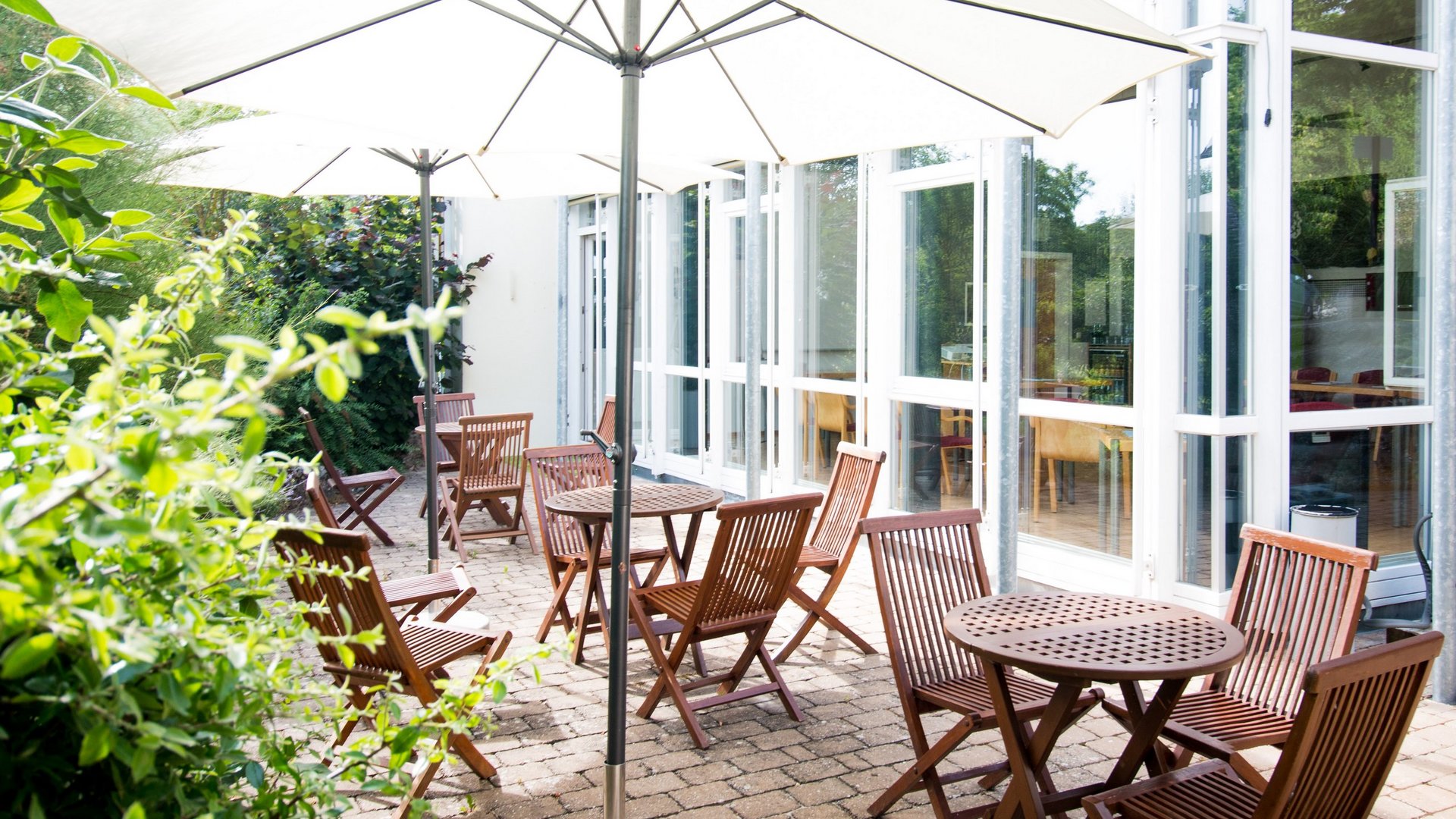 Tagungshotel Oberpfalz: Das Hotel für Deine Tagung Terrasse mit Holztischen, Stühlen und großen Sonnenschirmen bei Tageslicht