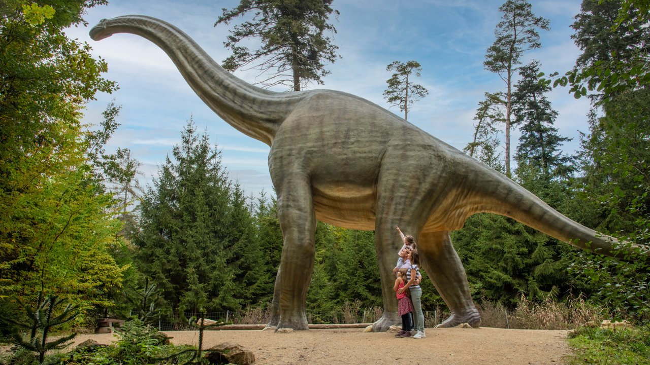 Familie steht vor einer großen Dinosaurier-Skulptur im Waldpark