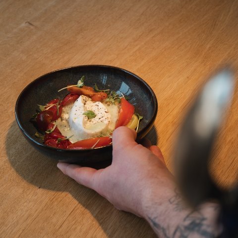 Restaurant in Parsberg: Gourmet genießen Hand hält Schüssel mit Burrata und Tomaten auf Holztisch