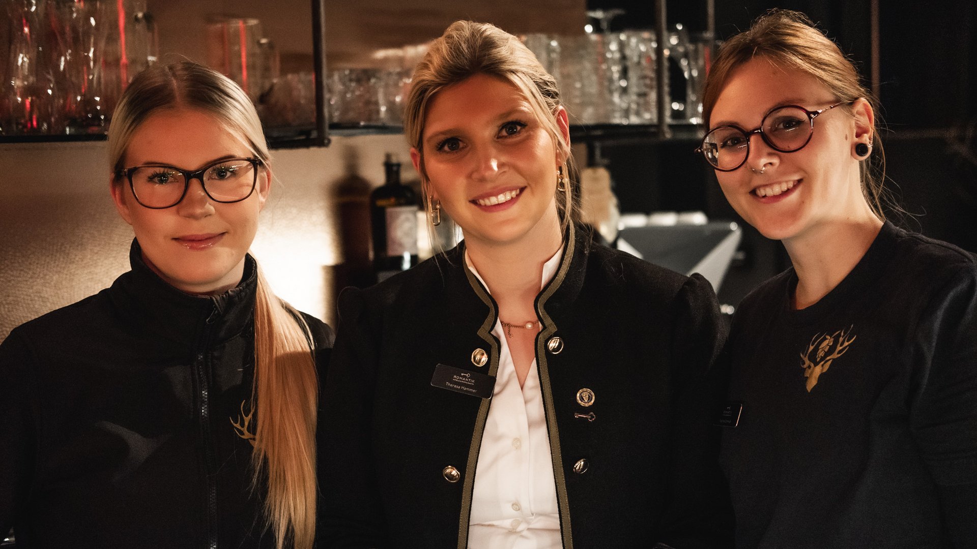 Hirschenblobb: Our bar Three smiling female staff in black uniforms at a bar