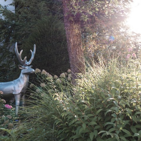 Tageswellness in der Oberpfalz Silberner Hirsch aus Metall steht im Garten zwischen Blumen und Bäumen