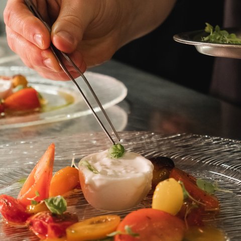 Restaurant in Parsberg: Gourmet genießen Hand platziert Basilikumblatt auf Burrata mit Tomaten auf Teller