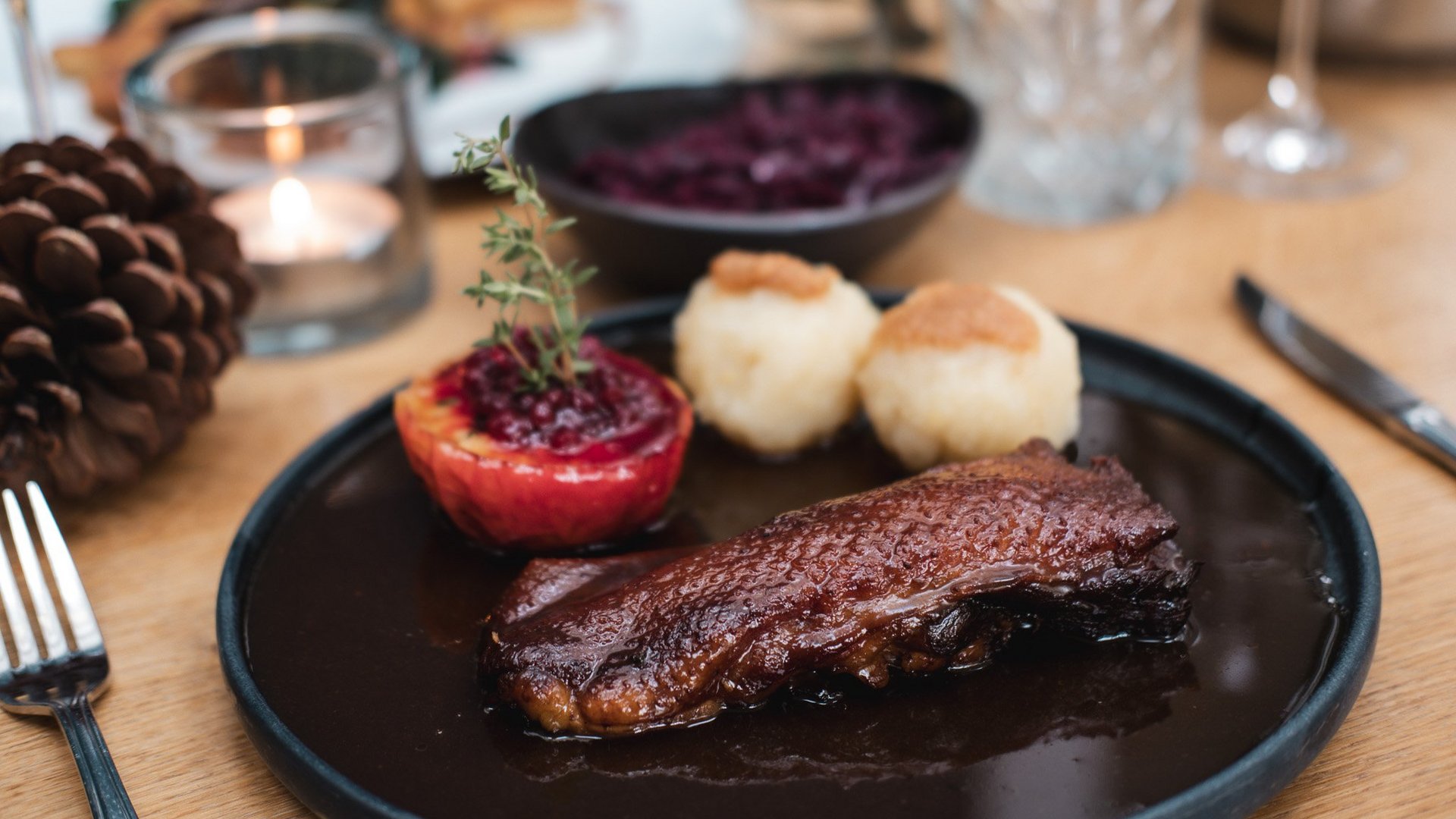 Christmas menus 2023 Table setting with game meat, stuffed apple, and dumplings on a black plate