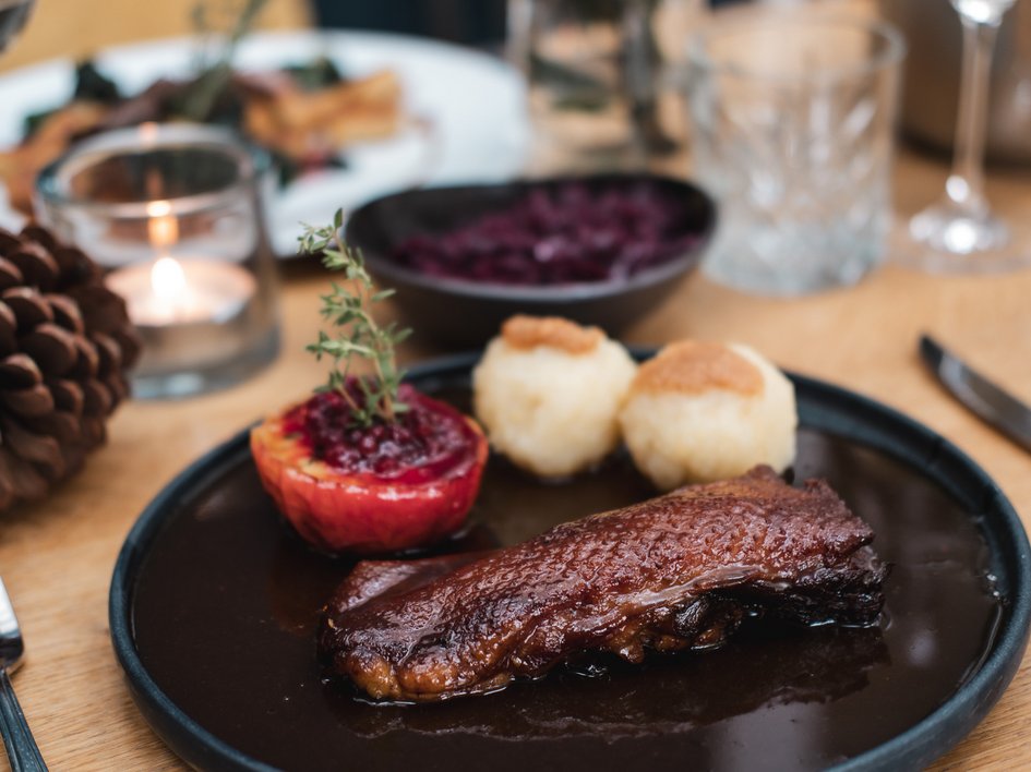 Gasthof Parsberg: Ein Gruß an den guten Geschmack Gedeckter Tisch mit Wildgericht, gefülltem Apfel und Klößen auf schwarzem Teller