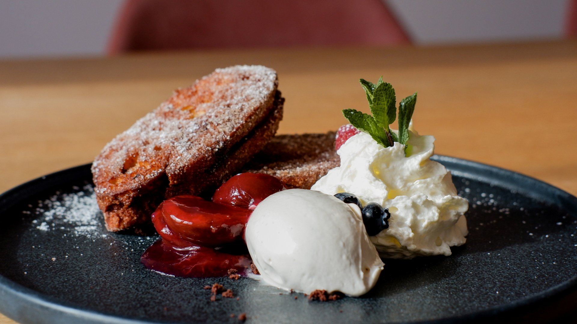 Gasthof Parsberg: Ein Gruß an den guten Geschmack Dessert mit Kuchen, Vanilleeis, Kirschen und Sahne mit Minzblatt auf schwarzem Teller