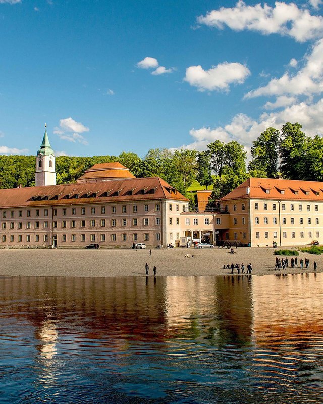 Golf holiday in Bavaria: top boss or beginner? Monastery on Danube shore with fishing boats and forested cliffs in background
