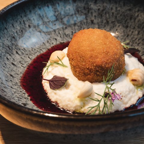 Restaurant in Parsberg: Gourmet genießen Panierter, gebratener Bällchen auf cremigem Püree mit Nüssen und Kräutern in schwarzer Schale