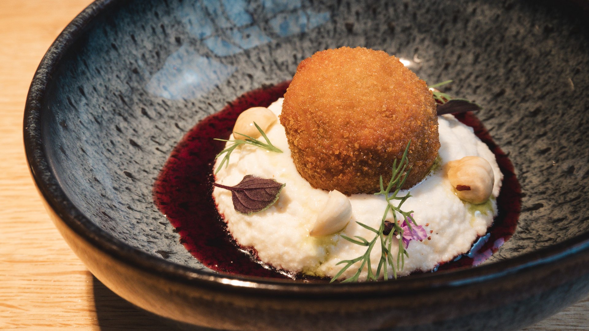 Restaurant in Parsberg: Gourmet genießen Panierter, gebratener Bällchen auf cremigem Püree mit Nüssen und Kräutern in schwarzer Schale