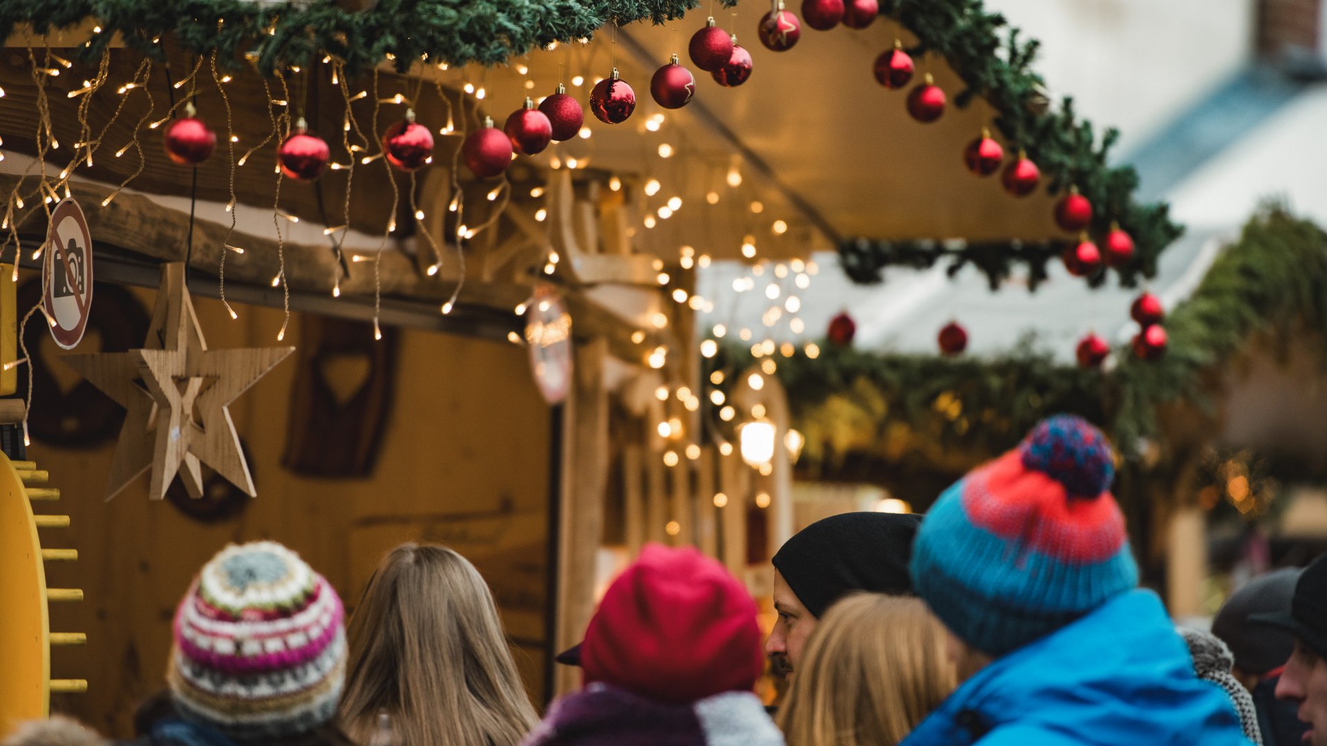 Weihnachtsmärkte Besucher vor einem festlich geschmückten Weihnachtsmarktstand mit roten Kugeln und Lichterketten