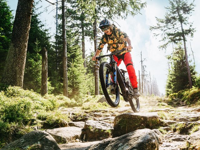 Romantik Hotel Hirschen: Bildergalerie Mountainbiker springt mit Helm und roter Hose auf felsigem Waldweg