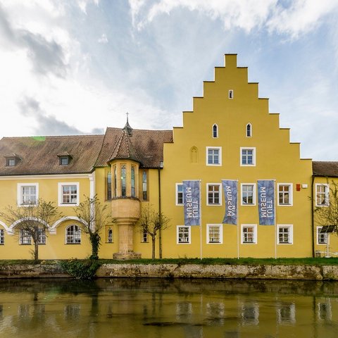 Hotels in Regensburg und Umgebung: kultur-trächtig! Gelbes historisches Gebäude am Wasser mit Treppengiebel und Fahnen