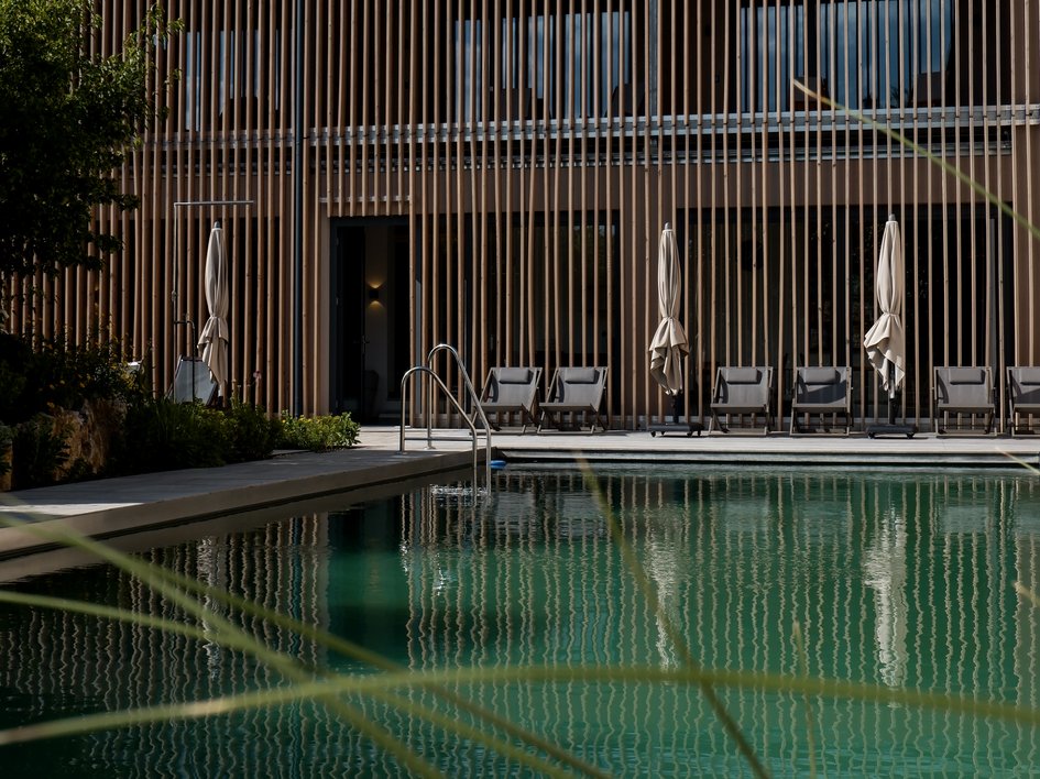 Nachhaltige Hotels in Deutschland gesucht? Schwimmbad mit Liegestühlen vor modernem Holzgebäude bei Tageslicht