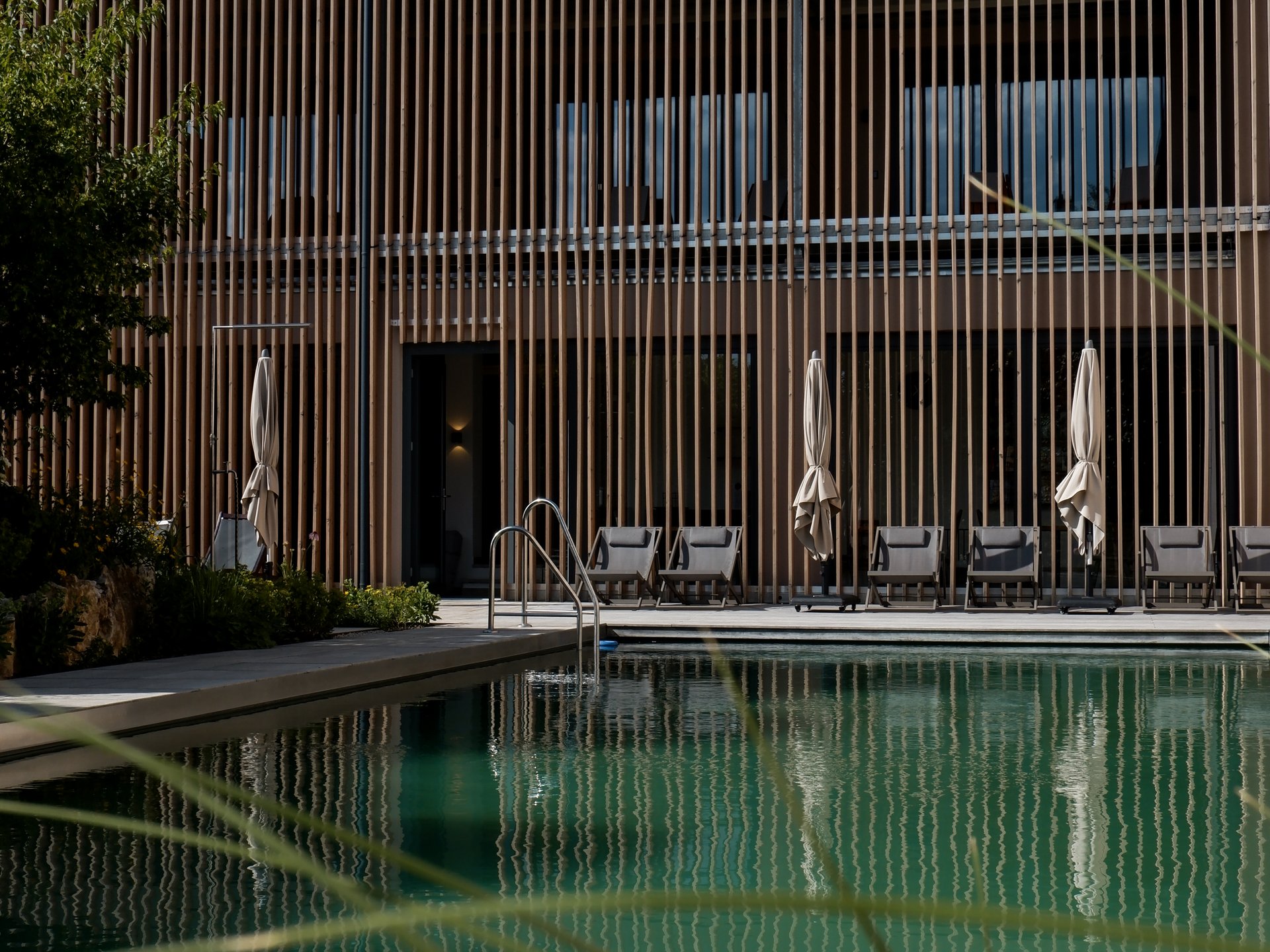 What we do. And why. Swimming pool with lounge chairs in front of modern wooden building in daylight