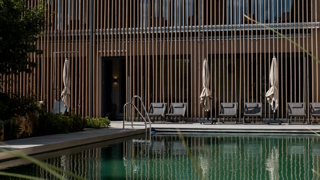 Badeseen Schwimmbad mit Liegestühlen vor modernem Holzgebäude bei Tageslicht