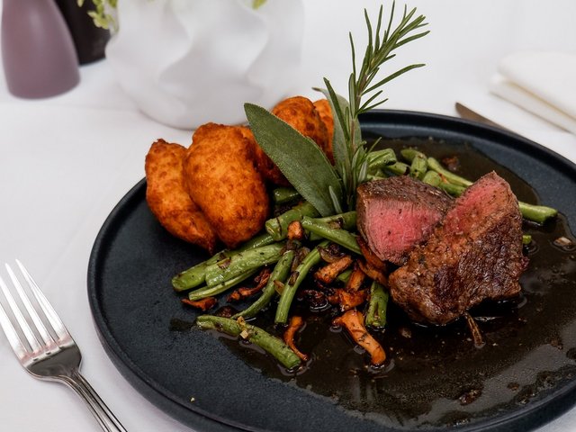 Romantik Hotel Hirschen: Bildergalerie Rindersteak mit grünen Bohnen und Bratkartoffeln auf schwarzem Teller