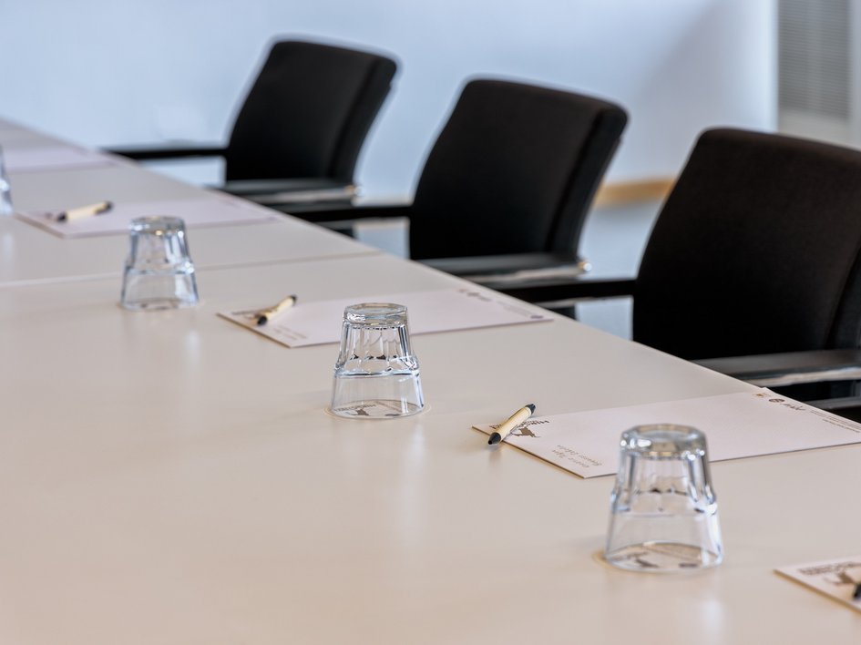 Leistungen und Preise für Tagungen und Konferenzen Konferenztisch mit Stühlen, Gläsern, Notizblöcken und Stiften vorbereitet