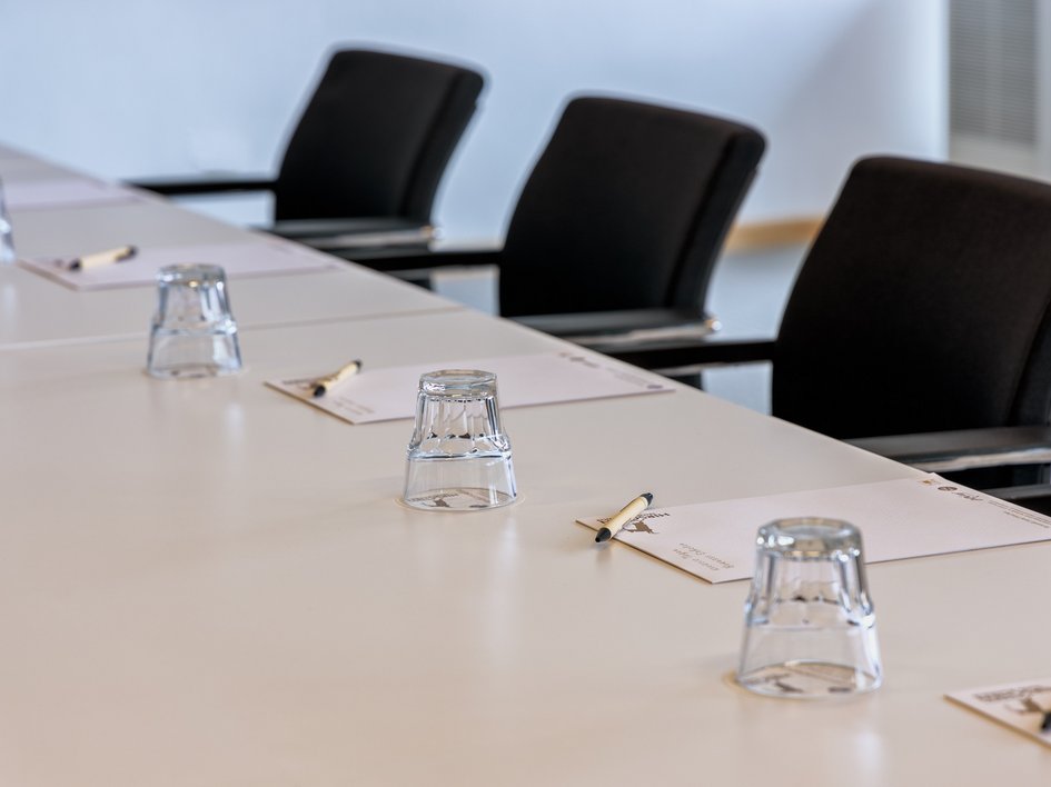 Leistungen und Preise für Tagungen und Konferenzen Konferenztisch mit Stühlen, Gläsern, Notizblöcken und Stiften vorbereitet