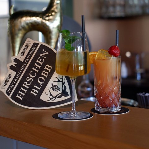 Hirschenblobb: Our bar Two cocktails and a deer figure with Hirschen Blobb sign on a bar counter