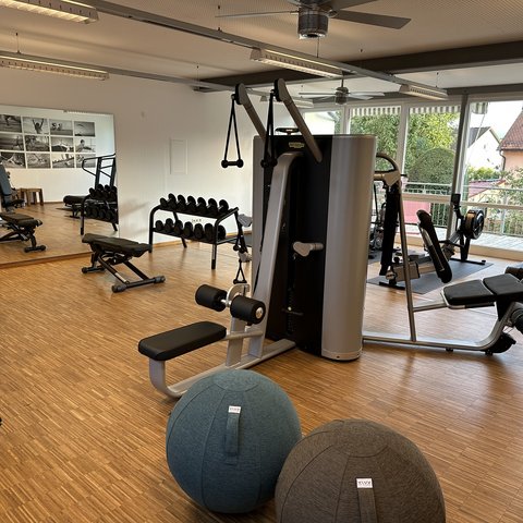 Tageswellness in der Oberpfalz Moderner Fitnessraum mit Geräten, Hanteln und Gymnastikbällen vor großem Fenster