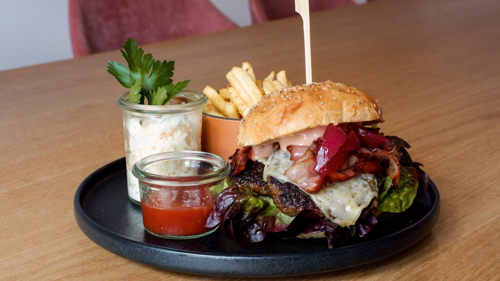 Guesthouse in Parsberg: A salute to great taste Burger with cheese, bacon, lettuce, fries and sauces on black plate