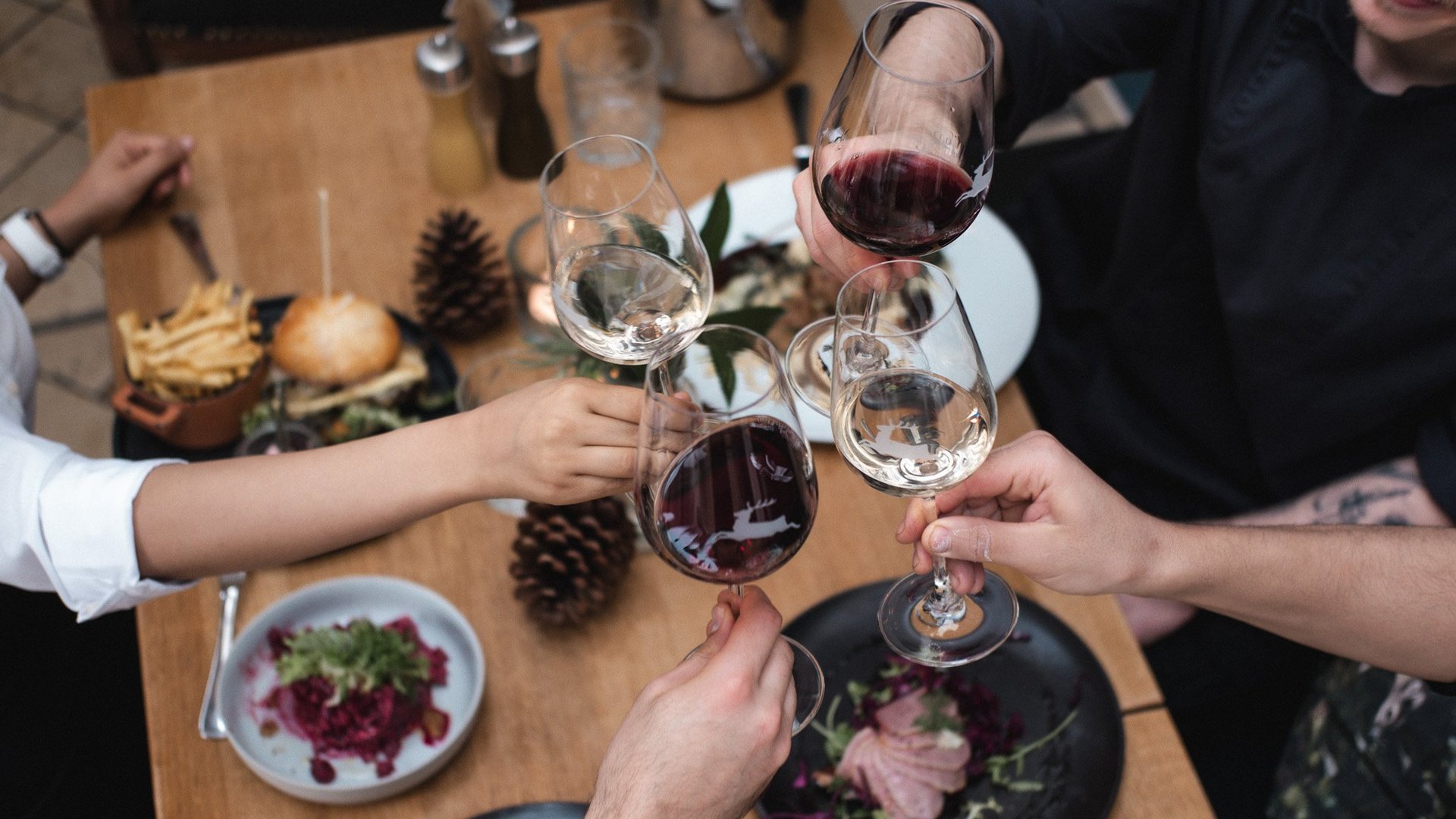 Gasthof Parsberg: Ein Gruß an den guten Geschmack Menschen stoßen mit Rot- und Weißweingläsern über einem gedeckten Tisch an