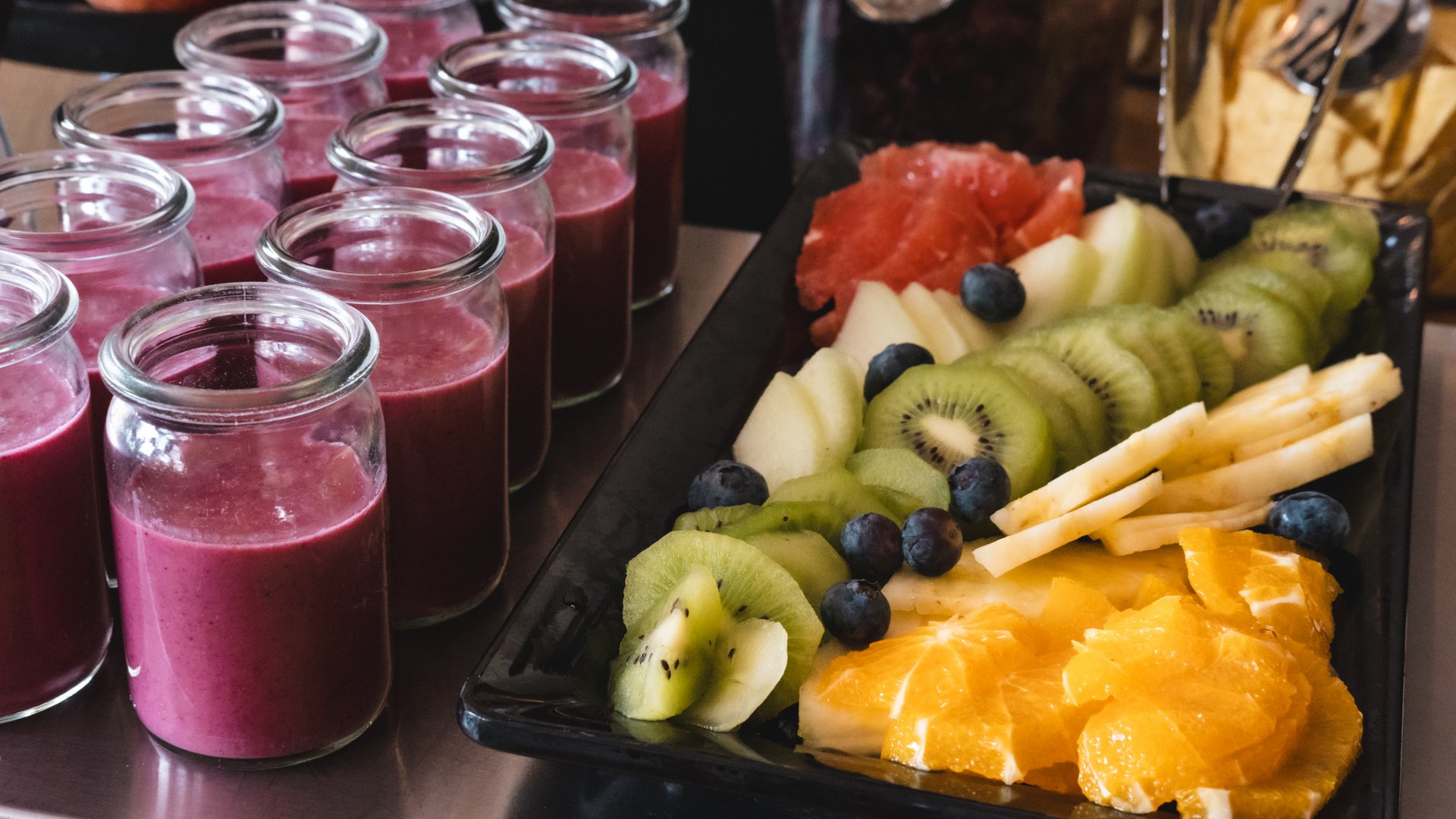 Tagung mit Mehrwert Gläser mit rotem Smoothie neben Teller mit unterschiedlichen frischen Obststücken
