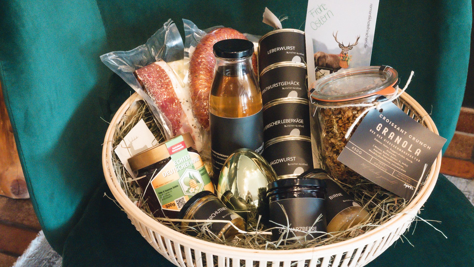 Nachhaltiges Hotel in Bayern mit Hirschenmanufaktur Geschenkkorb mit Wurst, Honig, Granola und Osterkarte auf grünem Stuhl