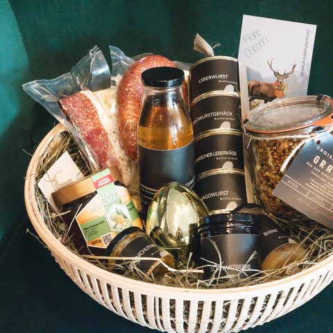 Nachhaltiges Hotel in Bayern mit Hirschenmanufaktur Geschenkkorb mit Wurst, Honig, Granola und Osterkarte auf grünem Stuhl
