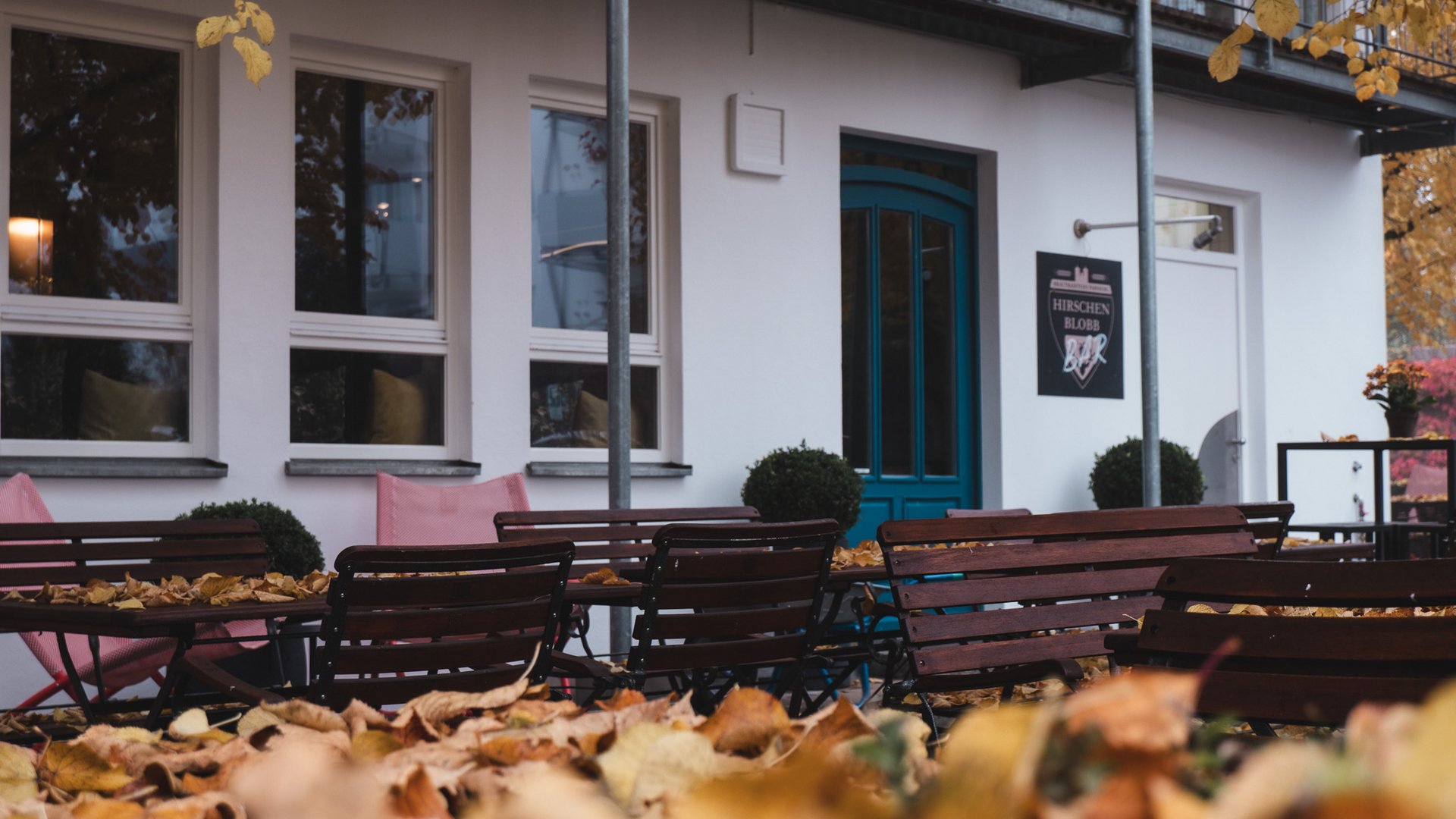 Hirschenblobb: unsere Bar Leere Sitzgelegenheiten mit Herbstblättern vor einem Café im Freien