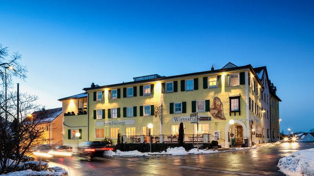 Romantik Hotel Hirschen: Blog Beleuchtetes gelbes Gebäude bei Abenddämmerung mit Schnee und Autos auf Straße