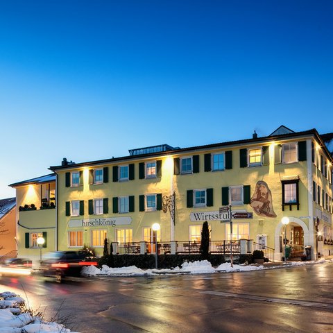Deine Anfrage im Romantik Hotel Hirschen Beleuchtetes gelbes Gebäude bei Abenddämmerung mit Schnee und Autos auf Straße