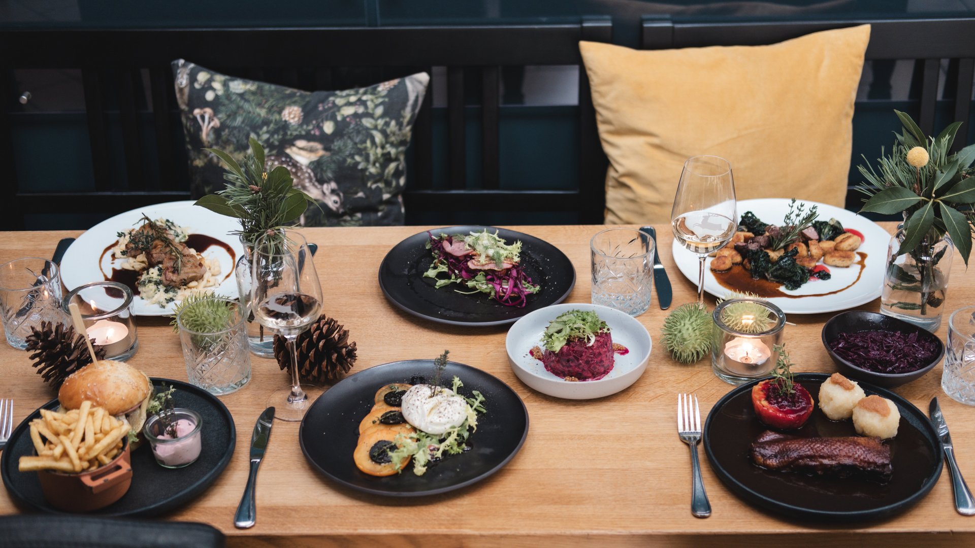 Variety of dishes on a wooden table with decorative pillows and candles