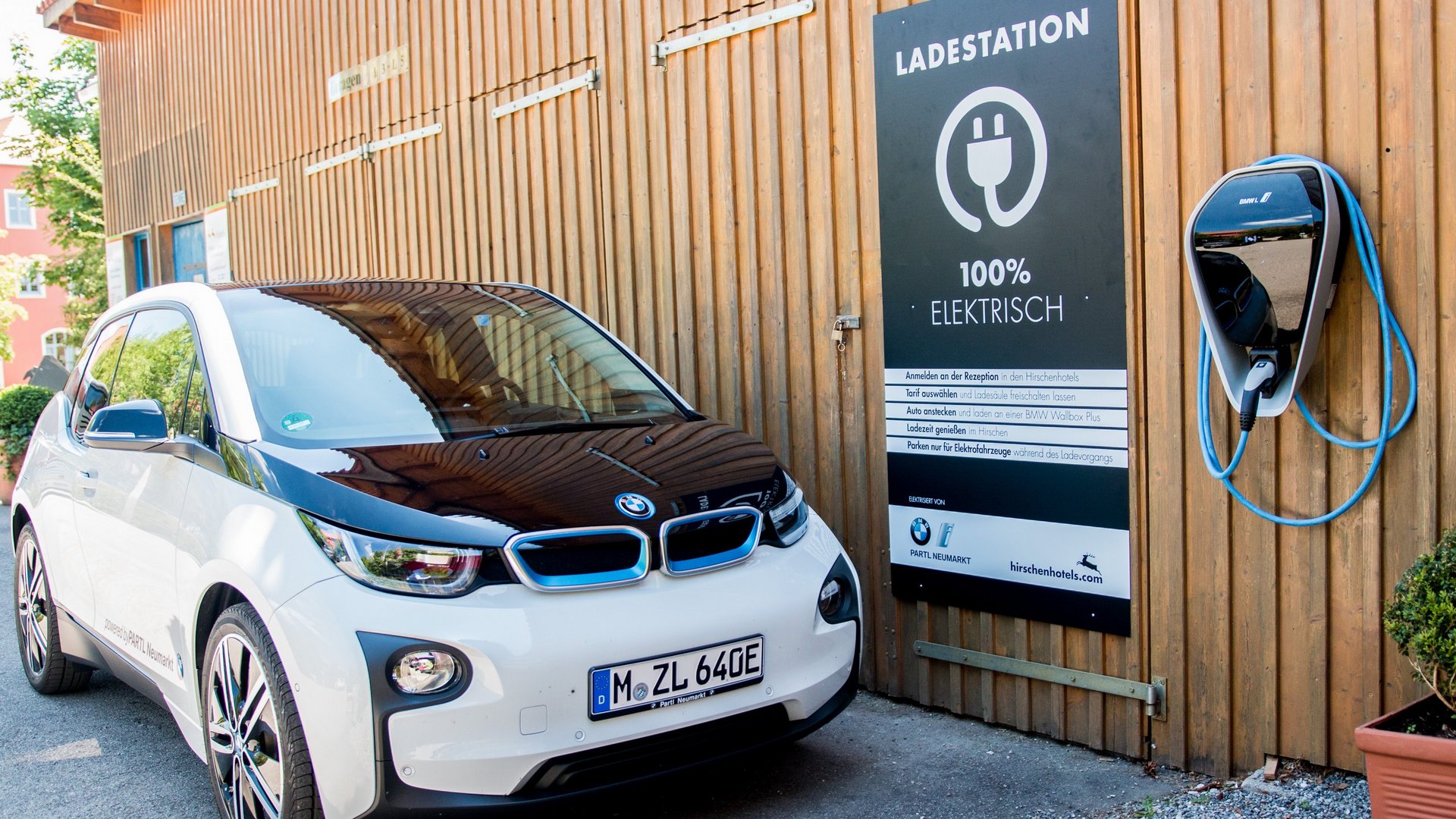 Nachhaltige Hotels in Deutschland gesucht? Elektroauto BMW i3 an Ladestation mit Schild 100% elektrisch