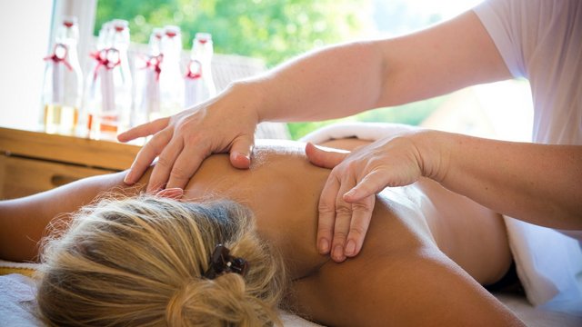 Romantik Hotel Hirschen: Blog Person erhält Rückenmassage in hellem Raum mit Glasflaschen im Hintergrund